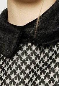 Svart sammet Peter Pan-krage ovanför ett mönster av svarta och vita stjärnformer på texturerad tyg. Närbild som visar detaljer och material.