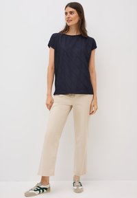 Top de manga corta azul marino con un patrón texturizado de zigzag, combinado con pantalones rectos beige y zapatillas verde grisáceo.