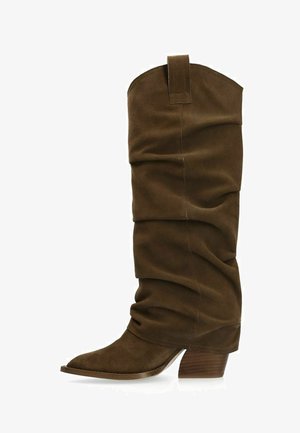 Botte haute jusqu'au genou en daim marron avec un design effondré, un bout pointu et un talon empilé. Comprend une boucle en haut pour faciliter l'accès.