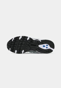 Semelle de chaussure New Balance noir et blanc avec un motif de crampons texturé et des accents bleus sur le talon, présentée sur un fond blanc.
