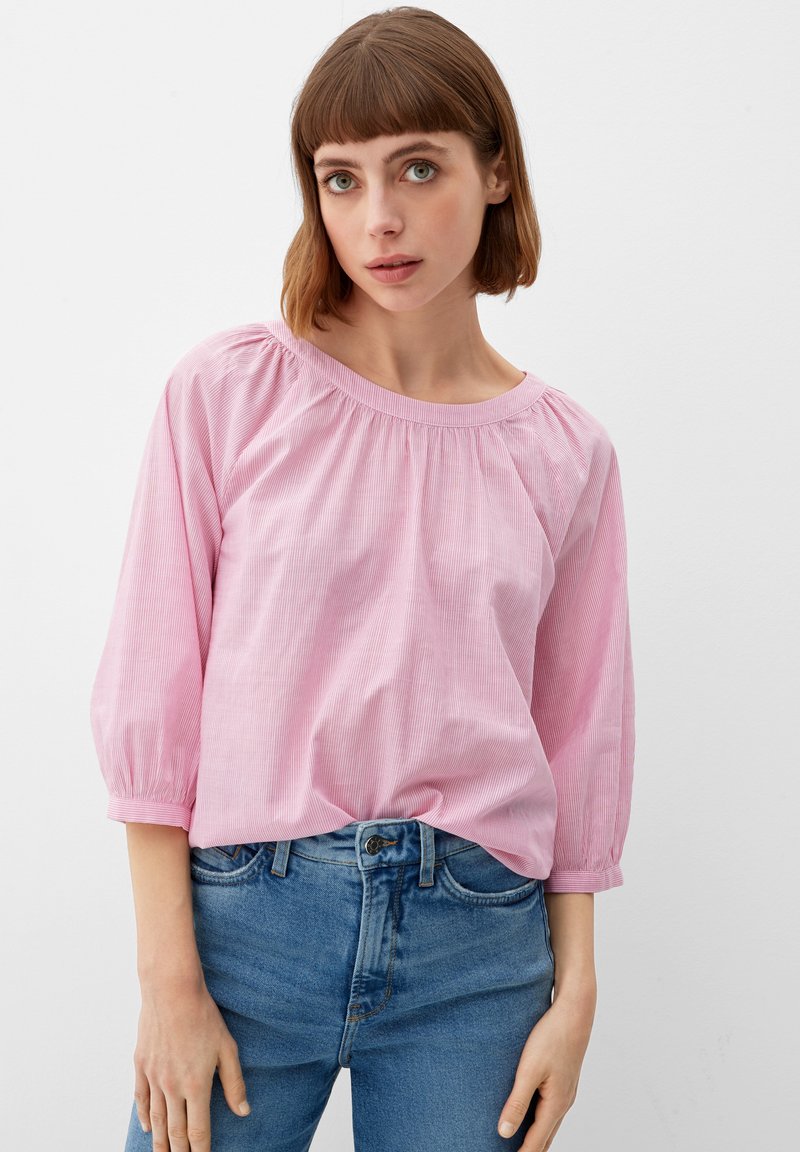 Roze gestreepte blouse met een ronde hals, geplooide schouderdetails, driekwartmouwen, gemaakt van een lichte stof. Gecombineerd met blauwe jeans.