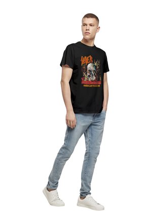 Black t-shirt featuring a colorful graphic with a skull and text, paired with light blue jeans and white sneakers. Model stands casually.
