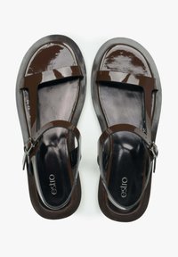 Bruine gepatineerde leren sandalen met een platte zool, voorzien van een T-band ontwerp, verstelbare enkelband en een gladde zwarte binnenkant.