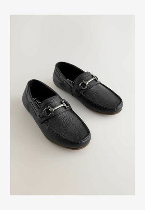 Czarne mokasyny ze skóry o fakturowanej powierzchni, z akcentami srebrnego metalu i przeszyciami wzdłuż krawędzi. Zaprojektowane z myślą o wygodzie zakładania na sucho.