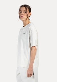 Biała bawełniana koszulka z krótkim rękawem, okrągłym dekoltem i małym haftowanym logo na piersi. Gładka faktura, luźny krój.