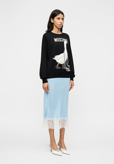 Μαύρο φούτερ με γραφικό χήνας και το κείμενο «Moschino», σε συνδυασμό με φούστα ανοιχτού μπλε με άσπρη δαντέλα. Άσπρα παπούτσια τύπου slip-on με τακούνι.