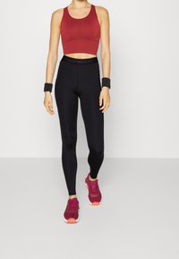 Röd kortärmad sporttop, högmidjade svarta leggings och vinröda löparskor med orange accenter; inkluderar svarta handledsstöd.