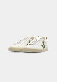 Hvite lær sneakers med grønne gummidetaljer, strukturert såle, flate lisser og avrundet tå. Minimalistisk design med logo.