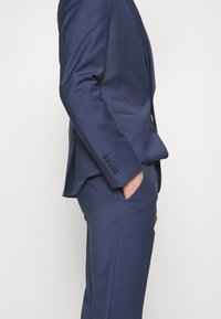 Navy blue tailored suit with a smooth texture, single-breasted jacket, notched lapels, and four-button cuff detailing; slim-fit trousers.