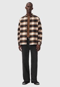 Svart och brun rutig skjorta i ett mjukt tyg, med krage och knappstängning, kombinerad med mörka jeans och svarta skor.