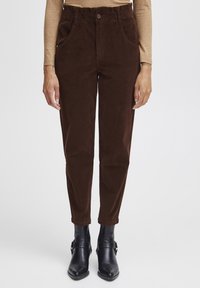 Brown corduroy pants with side pockets, tapered leg, and elastic waistband, paired with black ankle boots. Smooth texture, no visible patterns.