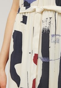 Robe à motifs présentant des formes abstraites en marine, rouge et violet sur un fond crème, avec un détail à la taille nouée et une texture de tissu douce.