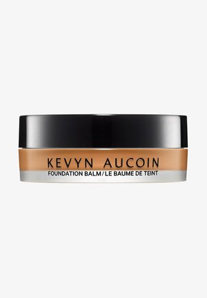 Kevyn Aucoin Foundation Balm in a round, clear container with a black lid. Smooth, creamy texture in a warm beige shade. Silver band details.