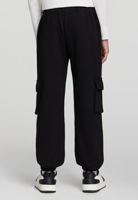 Czarne spodnie dresowe o luźnym kroju, z elastycznym pasem, bocznymi kieszeniami i ściągaczami na końcach nogawek. Wykonane z miękkiego materiału, charakteryzujące się minimalistycznym stylem.