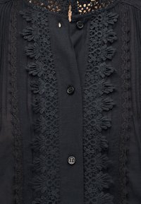 Μαύρο μπλουζάκι με κατακόρυφη διακόσμηση από δαντέλα με λουλούδια, τρία ορατά μαύρα κουμπιά και λεπτή δαντέλα στις άκρες σε διάφανο ύφασμα.