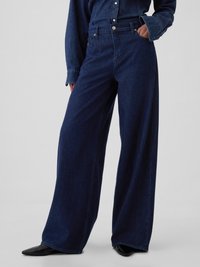 Jeans din denim de culoare albastră închisă, cu croi larg, talie înaltă, cusături subtile, accesorii metalice și buzunare laterale. Textură netedă.