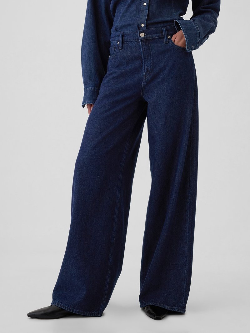 Jeans din denim de culoare albastră închisă, cu croi larg, talie înaltă, cusături subtile, accesorii metalice și buzunare laterale. Textură netedă.
