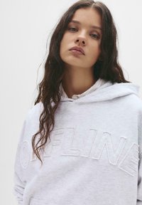Hoodie grigio chiaro con la scritta "OFFLINE" ricamata in un carattere testurizzato e in rilievo. Presenta un cappuccio con coulisse e una vestibilità casual.