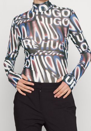 Top ajustado de manga larga con cuello alto y patrón abstracto multicolor en azul, rojo, blanco y negro, combinado con pantalones negros.