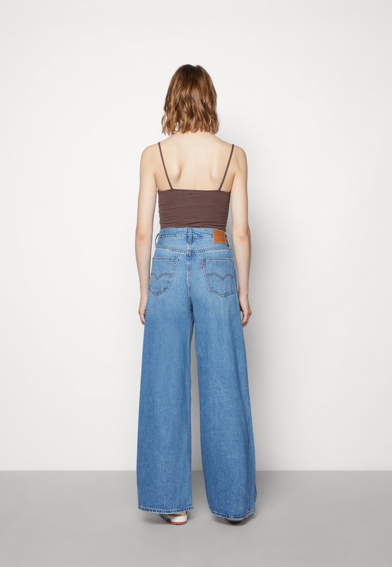 Jean en denim bleu à jambe large et taille haute, avec une étiquette en cuir marron au dos et un design classique à 5 poches.