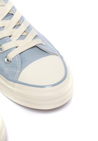 Hele helesinine canvas toss, millel on kreemivärvi kummist varbad ja tallad, valged paelad ja hõbedased silmad, tekstuuriga kummist välistald.