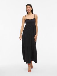 Rochie maxi neagră cu bretele subțiri, design în straturi și textură netedă. Pur și simplu cu sandale roșii cu curea.