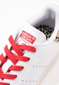 Weißes Leder-Sneaker mit roten Schnürsenkeln und einem Leopardenmuster-Futter. Verfügt über ein Logo-Patch auf der Zunge mit "adidas STAN SMITH."