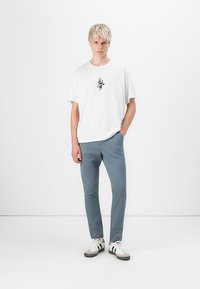 Hvit bomulls t-skjorte med svart grafikk, blå bukser og hvite sneakers med svarte detaljer. Antrekket har en avslappet passform.