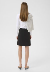 Jupe noire en forme de A, longueur genoux, associée à un haut blanc à manches longues. Un pull gris clair drapé sur les épaules, en tissu doux, au design simple.