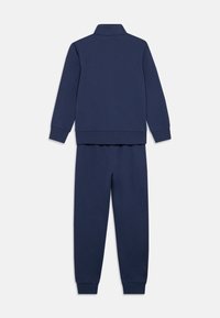 Σκούρο μπλε φόρμα με μπλουζάκι με γιακά και παντελόνι που ταιριάζει. Απαλό ύφασμα, ριμπ μανσέτες και μέση. Απλός σχεδιασμός, χωρίς σχέδια ή διακοσμητικά στοιχεία.