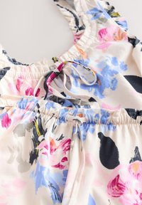 Tissu à motif floral avec fronces élastiques et cordons noués dans des nuances de rose, bleu, noir et orange sur un fond clair.