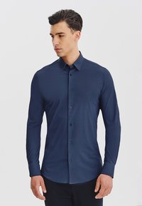 Granatowa koszula zapinana na guziki z długim rękawem, z subtelnym wzorem teksturowym, dopasowany krój i klasyczny kołnierzyk, z pasującymi guzikami.