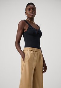 Must musta kehakujuline bodysuit, millel on võtmeaugu detail, koos beežide laiade pükstega, millel on elastne vöökoht ja külgtaskud.