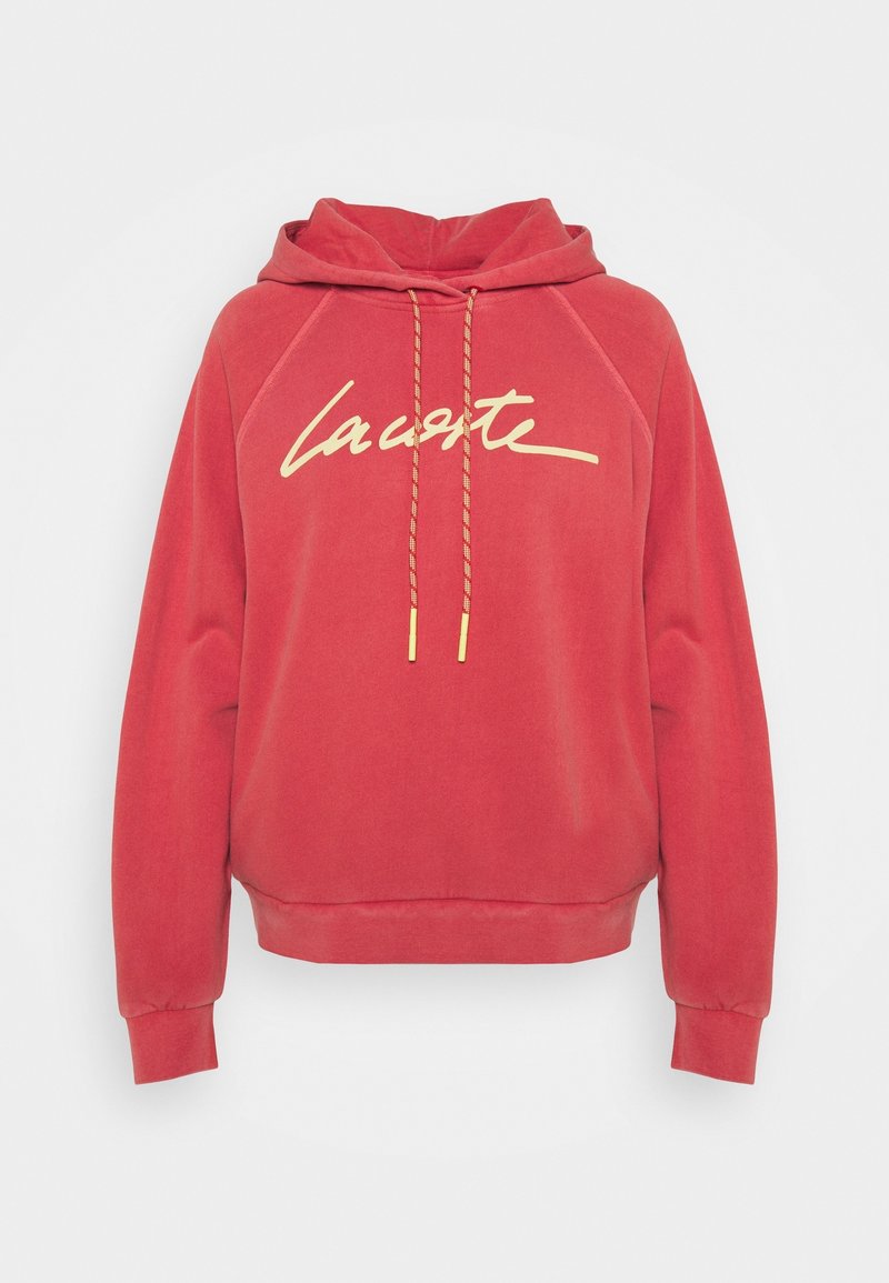 Sweat à capuche rouge à manches longues, inscription jaune "lacoste" sur le devant, et cordons rouges assortis avec embouts jaunes.