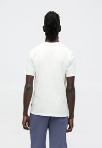 Bílé bavlněné tričko s kulatým výstřihem, krátkými rukávy a jednobarevným zadním dílem. Na lemu je malá černá etiketa.