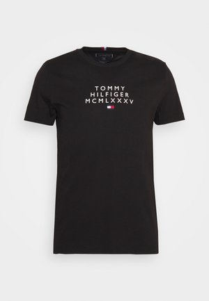 Czarny T-shirt z krótkim rękawem i okrągłym dekoltem, z białym napisem "Tommy Hilfiger MCMLXXXV" oraz małym czerwono-biało-niebieskim logo Tommy Hilfiger na piersi.
