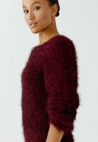 Bordeauxfarbener Pullover mit einer flauschigen, strukturierten Oberfläche. Er verfügt über einen weiten Ausschnitt und enganliegende Bündchen, die für einen bequemen Sitz sorgen.