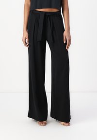 Wide-leg black trousers with a high waist, pleats, and a fabric tie belt. Smooth texture with a relaxed fit.
