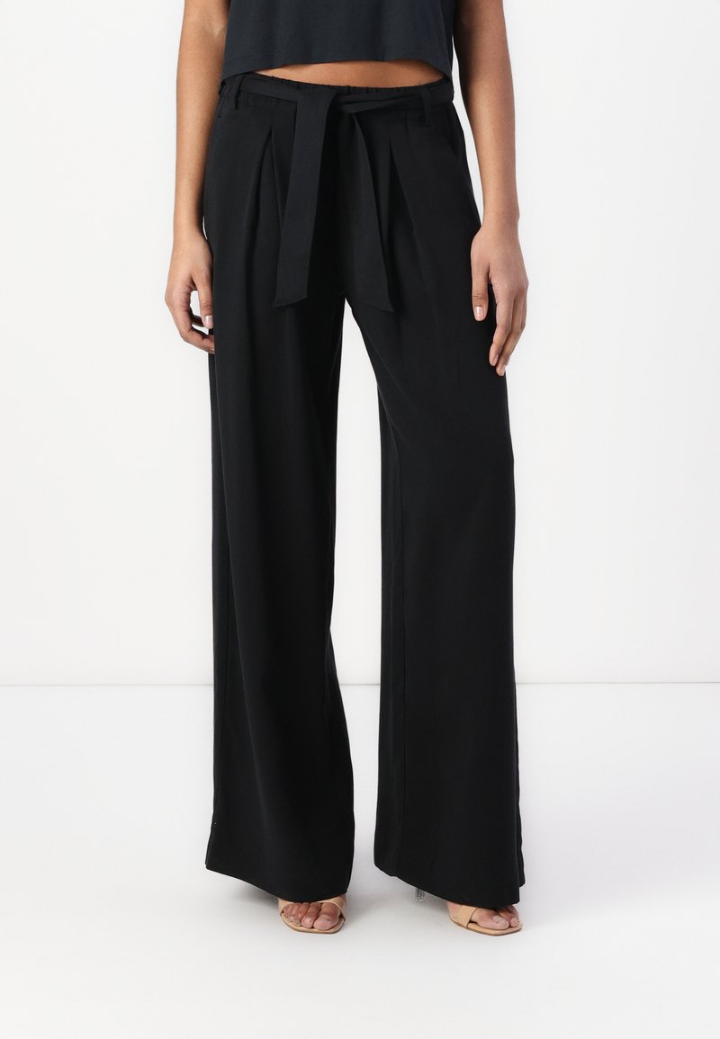 Wide-leg black trousers with a high waist, pleats, and a fabric tie belt. Smooth texture with a relaxed fit.