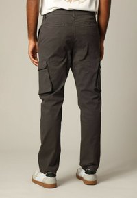 Grijze cargobroek met zijzakken, elastische tailleband en een relaxte pasvorm. Draagt met witte en zwarte sneakers tegen een lichte achtergrond.