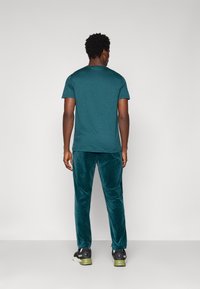 Miętowy t-shirt z okrągłym dekoltem i krótkimi rękawami, zestawiony z miękkimi, welurowymi spodniami dresowymi w tym samym kolorze. Czarne sneakersy z zielonymi akcentami dopełniają całość.