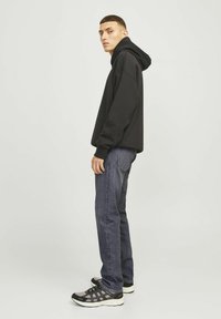 Un sweat à capuche noir avec une coupe décontractée, associé à un jean sombre et des chaussures de sport grises avec des accents noirs et une tige en maille texturée.