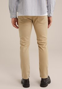 Khaki slim-fit byxor i en mjuk bomullsblandning, med bakfickor med subtila sömdetaljer och svarta skor synliga längst ner.