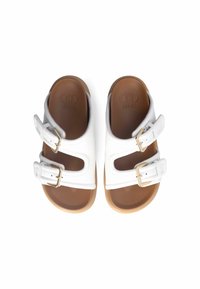 Sandales blanches avec deux boucles réglables, présentant des découpes. La semelle est marron avec une texture lisse. Matériau synthétique durable.