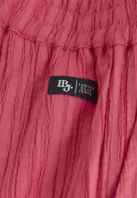 Różny, teksturowany materiał z pionowymi fałdami. Zawiera czarną metkę z napisem "IBJ. INDIAN BLUE JEANS." Miękka tkanina o pomarszczonym wyglądzie.