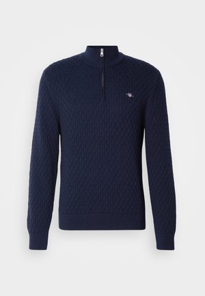 Suéter azul marino de cuello alto con cremallera, patrón de diamante texturizado, puños y dobladillo acanalados, que presenta un pequeño emblema de logo.