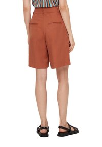 Rustkleurige, knielange shorts met een getailleerde pasvorm. Heeft achterzakken en een gladde textuur, gecombineerd met zwarte sandalen.
