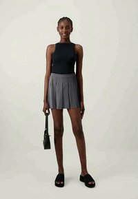 Svart tank topp, grå plisserte skjørt, svarte platå sandaletter. Modellen holder en liten svart veske. Enkelt design, glatt stoff, allsidige farger.