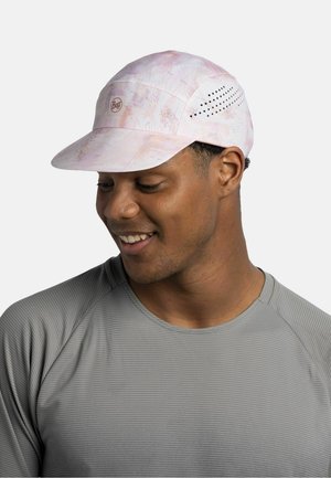 Man smiling, wearing a light pink patterned cap with ventilation holes and a gray textured long-sleeve shirt, looking down to the left.