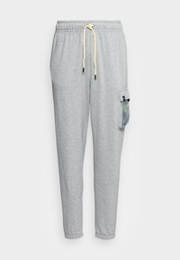 Graue Jogginghose mit einem Kordelzugbund, elastischen Bündchen und einer Seitentasche mit einem Netzdesign und hervorgehobenen Details in Schwarz.